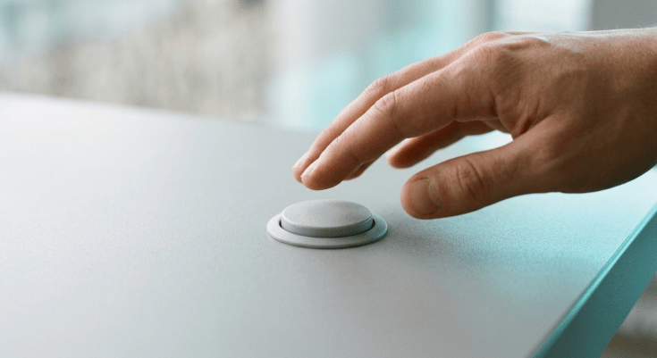 A single hand poised just above a plain unmarked button on a clean light gray surface, about to press it.