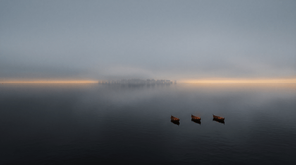 three small empty boats drifting on wide dark water at dawn, dwarfed by the sea and sky towards a roman fleet,